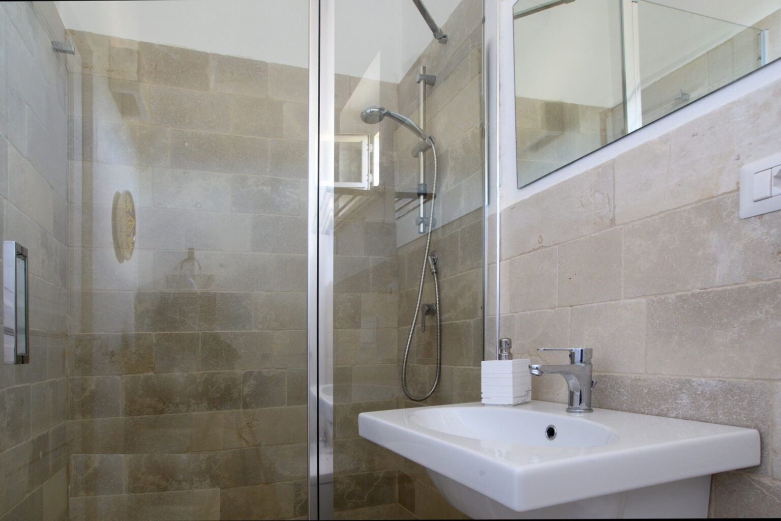 Modern bathroom featuring a glass shower enclosure, a sleek sink with a contemporary faucet, and beige tiled walls for a clean and stylish look. | Only on SopranoVillas