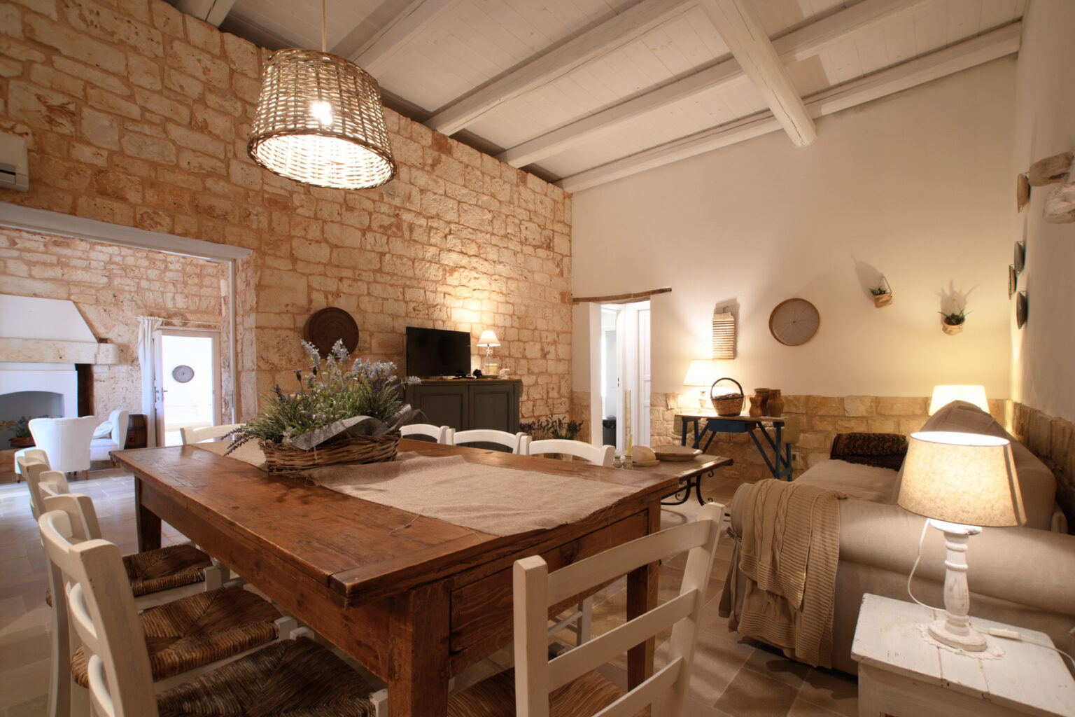 Cozy living room and dining area featuring a rustic wooden table, comfortable seating, and warm lighting, with stone walls and a high ceiling, creating an inviting atmosphere. | Only on SopranoVillas