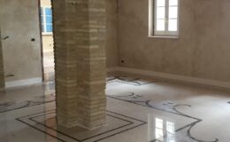 Interior view of an elegantly designed room featuring polished marble flooring with intricate patterns, a decorative column, and natural light streaming through windows, showcasing a modern yet classic aesthetic.