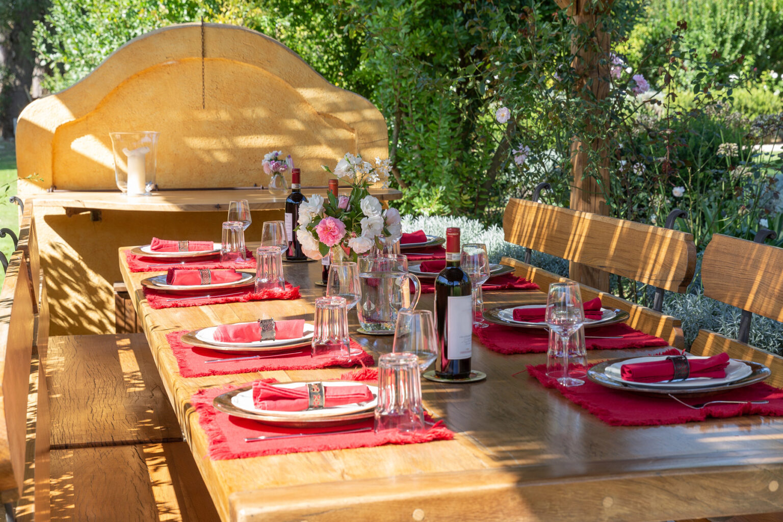 Outdoor dining setup featuring a wooden table elegantly arranged with red tablecloths, glassware, plates, and floral centerpieces, ideal for al fresco gatherings and special occasions. | Only on SopranoVillas