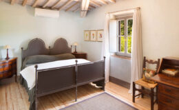 Cozy bedroom featuring a double bed with a dark metal frame, wooden furniture, a large window with natural light, and rustic decor elements. Ideal for a relaxing getaway or home inspiration.