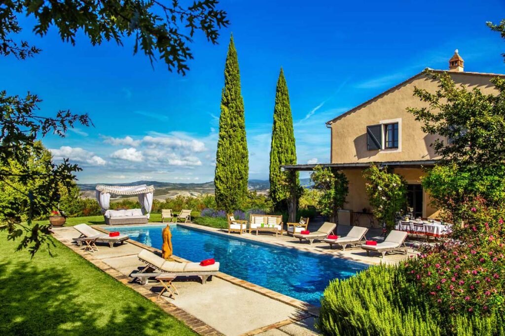 Luxury villa with a swimming pool surrounded by lush greenery and tall cypress trees, featuring sun loungers and a scenic view of the sky. Ideal for relaxation and outdoor gatherings. | Only on SopranoVillas