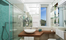 Modern bathroom design featuring a glass shower, a sleek wooden countertop with a round sink, and large windows providing natural light. The walls are adorned with turquoise tiles, enhancing the contemporary aesthetic.
