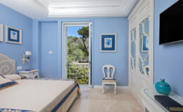 Cozy blue-themed bedroom featuring a comfortable bed, elegant decor, and a view of the garden through a glass door, complemented by modern furnishings and a wall-mounted TV.