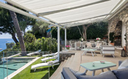 Luxury outdoor living space featuring a shaded patio, modern lounge furniture, and a beautiful view of the pool and ocean. Ideal for relaxation and entertaining.
