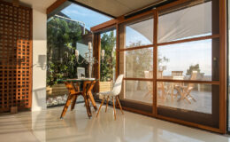 Modern interior with a wooden dining table and white chairs, featuring large glass doors that open to a garden view, showcasing natural light and contemporary design elements.