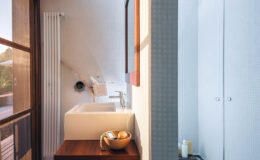 Modern bathroom interior featuring a stylish sink, wooden countertop with decorative bowl, and minimalistic storage options. Natural light enhances the clean lines and contemporary design, creating a serene atmosphere.