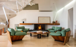 Modern living room featuring green contemporary sofas around a circular wooden coffee table, with a fireplace as the focal point, and minimalist decor.
