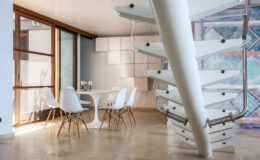 Modern interior design featuring a spiral staircase, a dining area with white chairs and a round table, and large windows allowing natural light to illuminate the space.