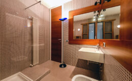 Modern bathroom featuring a walk-in shower, sleek sink with a contemporary vanity, and stylish lighting fixtures. The design incorporates warm wood accents and textured tiles, creating an inviting atmosphere.