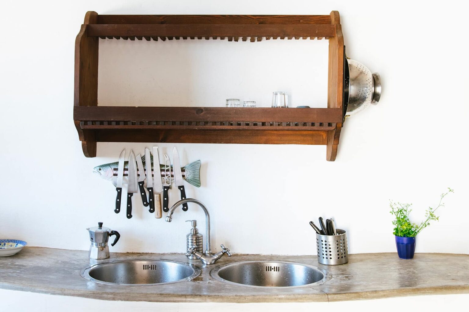 Modern kitchen featuring a wooden knife rack above a double stainless steel sink, with various kitchen utensils and a small plant on the countertop. | Only on SopranoVillas