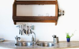 Modern kitchen featuring a wooden knife rack above a double stainless steel sink, with various kitchen utensils and a small plant on the countertop.