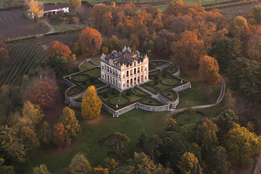 Aerial view of a stunning historic mansion surrounded by colorful autumn foliage, featuring manicured gardens and pathways. The elegant architecture contrasts with the vibrant seasonal landscape, highlighting the beauty of nature and heritage. | Only on SopranoVillas