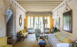 Bright and airy living room featuring yellow accents, a mix of vintage and modern furniture, and large windows that invite natural light. The room includes a comfortable sofa, stylish armchairs, and decorative artwork, creating a cozy and inviting atmosphere.