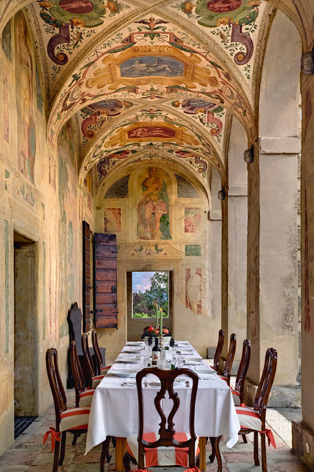 Interior view of a historic building featuring beautifully preserved frescoes on the walls and ceiling, with a wooden door partially open, revealing a scenic outdoor view. | Only on SopranoVillas