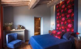 Cozy bedroom featuring a blue bedspread, floral accent wall, wooden beams, and stylish furniture, creating a warm and inviting atmosphere. Ideal for relaxation and comfort.