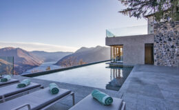 Modern luxury villa with an infinity pool overlooking a mountain landscape at sunset, featuring lounge chairs and a sleek design.