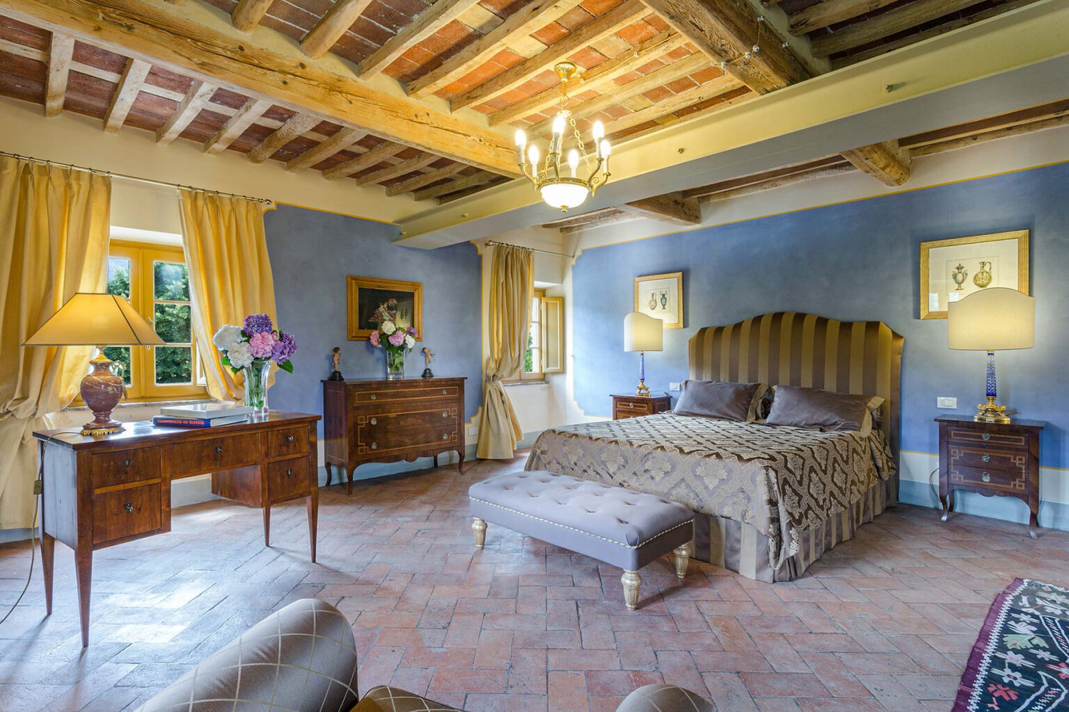 Luxurious bedroom with a king-sized bed, elegant furnishings, warm yellow curtains, and a chandelier, creating a cozy and inviting atmosphere. Perfect for a relaxing getaway or a romantic retreat. | Only on SopranoVillas