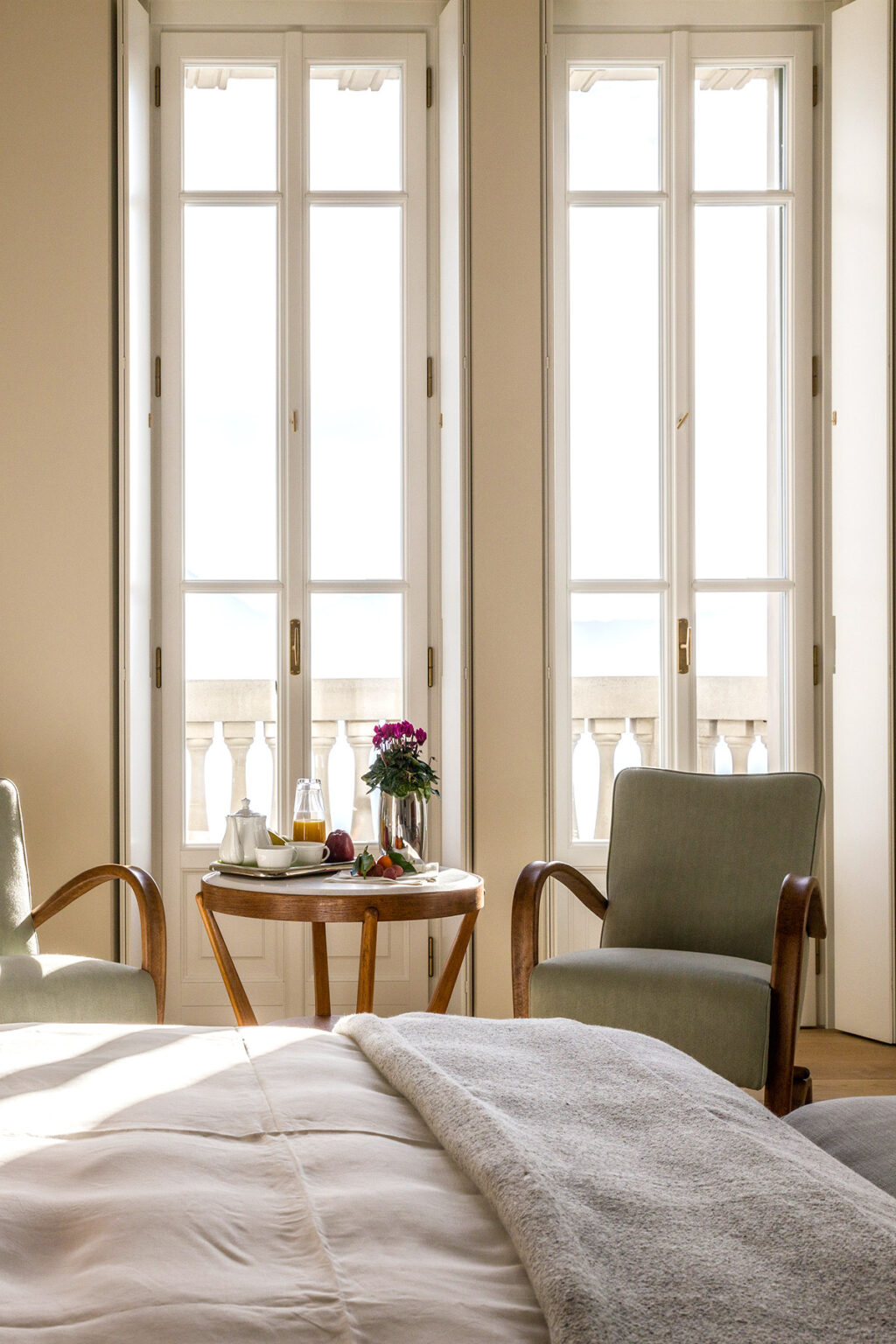 Cozy indoor seating area featuring two chairs and a small table with a vase of flowers, fruit, and a beverage, illuminated by natural light from large windows. Ideal for relaxation and enjoying a view. | Only on SopranoVillas