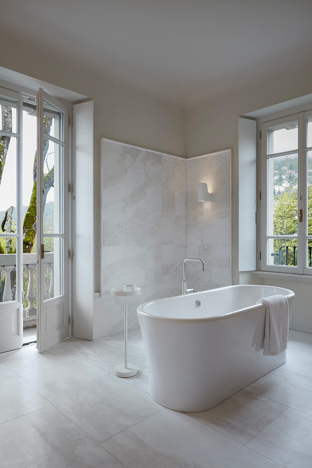 Modern bathroom featuring a freestanding white bathtub, large windows with natural light, and elegant marble walls, creating a serene and inviting atmosphere. | Only on SopranoVillas