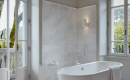Modern bathroom featuring a freestanding white bathtub, large windows with natural light, and elegant marble walls, creating a serene and inviting atmosphere.