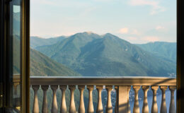 Scenic mountain view from a balcony with a decorative railing, showcasing lush green hills under a clear sky.