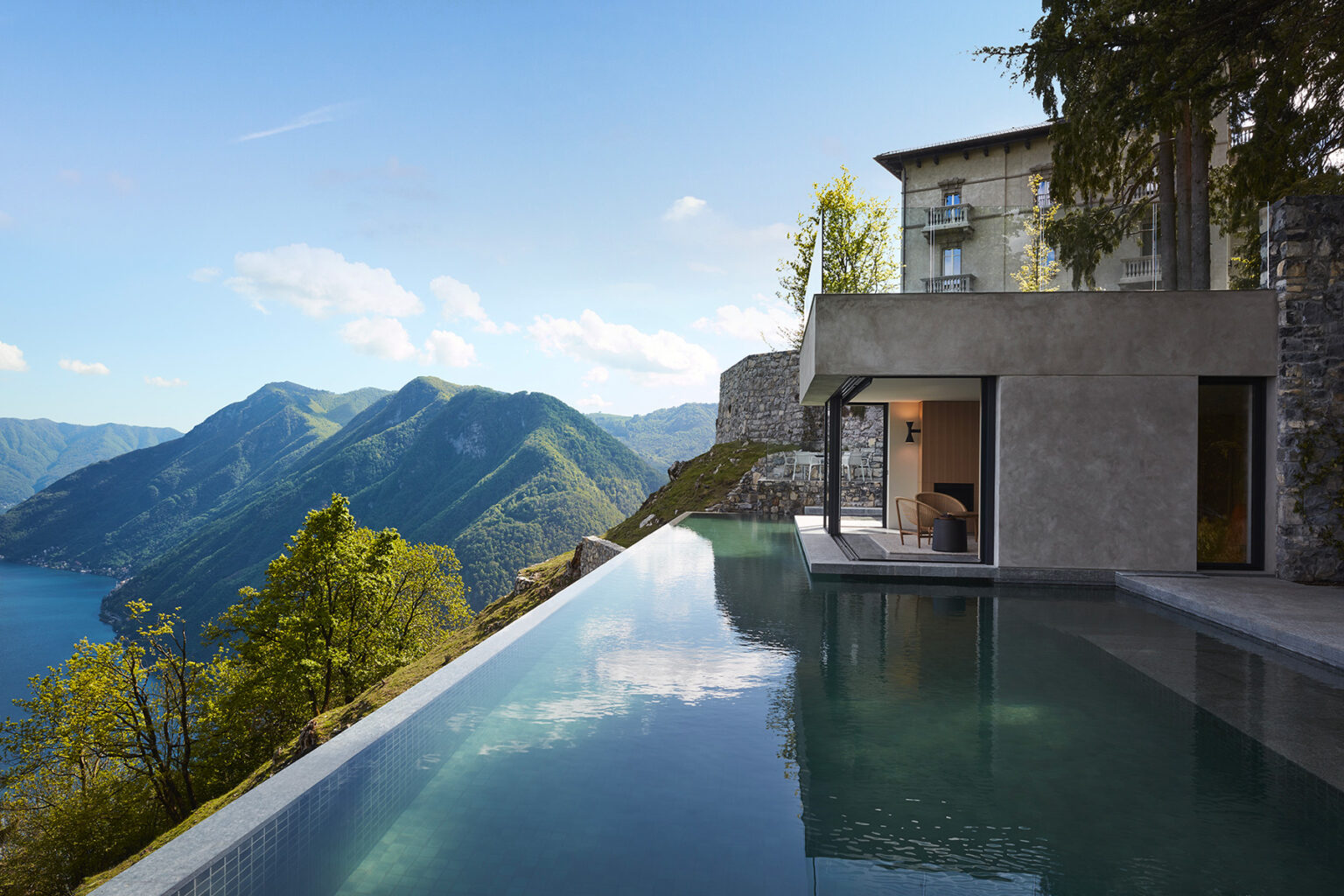 Modern luxury villa with an infinity pool overlooking a scenic mountain landscape and a tranquil lake under a clear blue sky. | Only on SopranoVillas