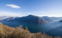 Panoramic view of a serene lake surrounded by mountains under a clear blue sky, showcasing the natural beauty of the landscape.