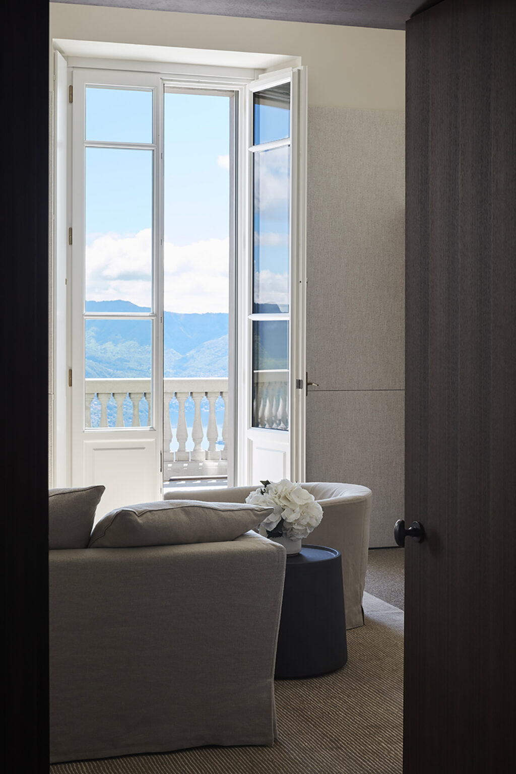 Interior view of a stylish room featuring a cozy seating area, an open balcony door with scenic mountain views, and decorative elements like a flower arrangement, creating a serene and inviting atmosphere. | Only on SopranoVillas