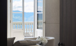 Interior view of a stylish room featuring a cozy seating area, an open balcony door with scenic mountain views, and decorative elements like a flower arrangement, creating a serene and inviting atmosphere.