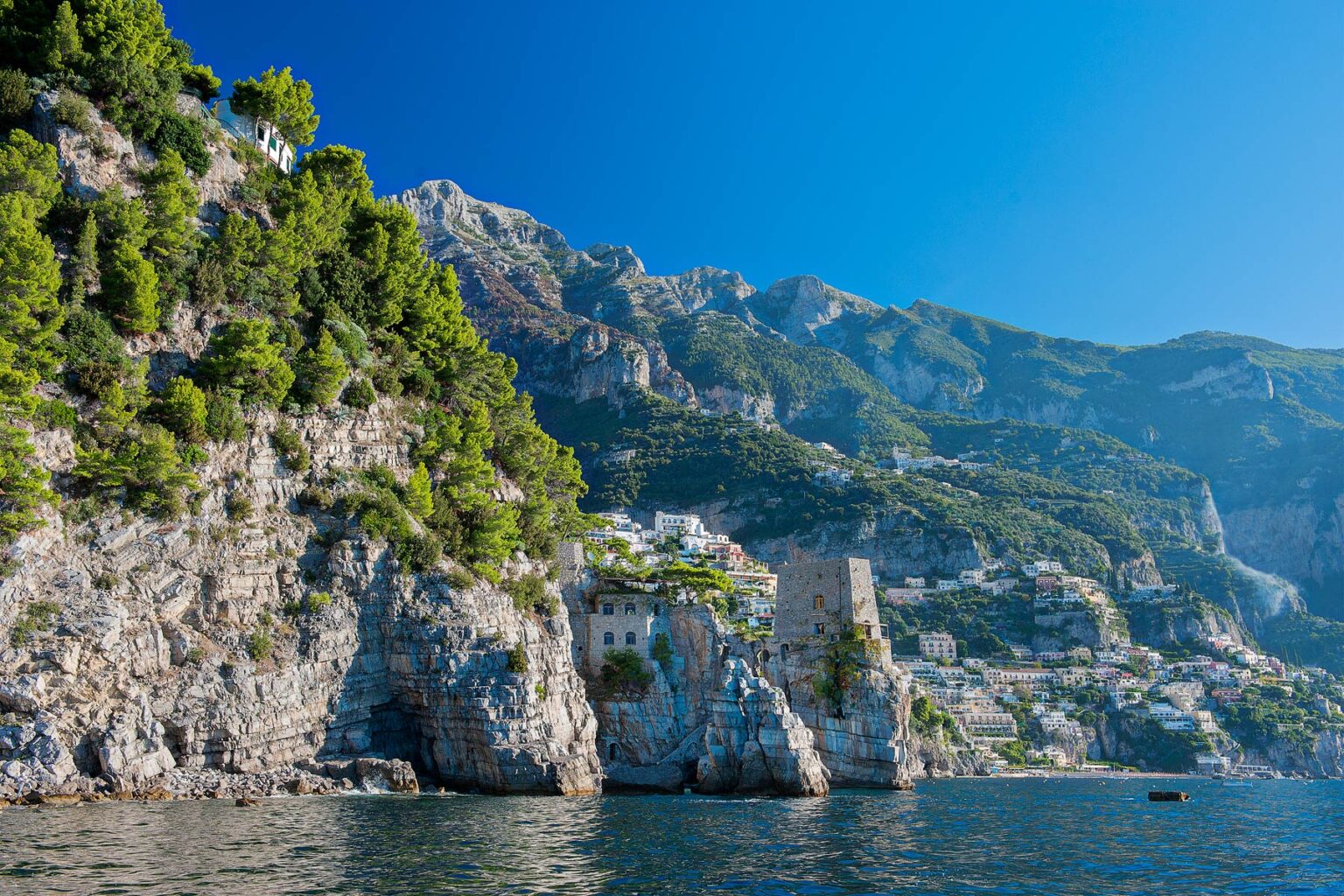 Scenic view of the Amalfi Coast featuring dramatic cliffs, lush greenery, and picturesque coastal villages under a clear blue sky. | Only on SopranoVillas
