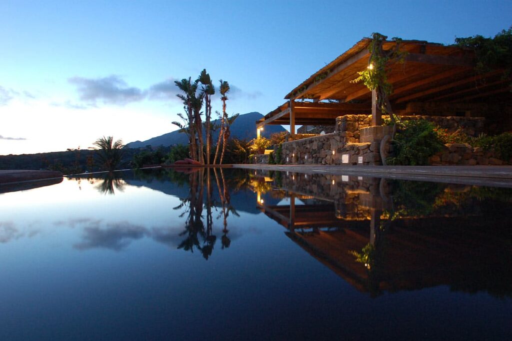 Luxury villa with modern architecture and infinity pool reflecting the sunset, surrounded by lush greenery and mountains in the background. Perfect for a serene getaway. | Only on SopranoVillas