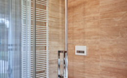 Modern bathroom interior featuring a glass shower enclosure, sleek chrome fixtures, and warm-toned tiled walls, highlighting a contemporary design aesthetic.