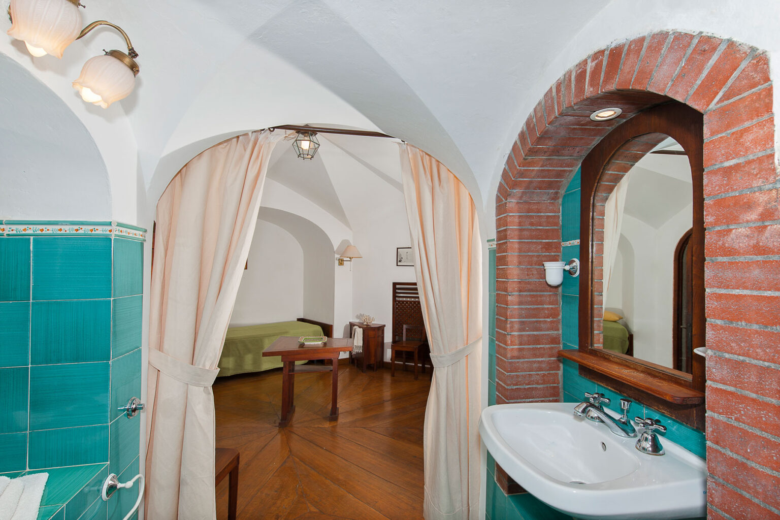 Spacious bathroom with turquoise tiles, a modern sink, and a stylish mirror, leading to a cozy room featuring wooden furniture and warm lighting. | Only on SopranoVillas