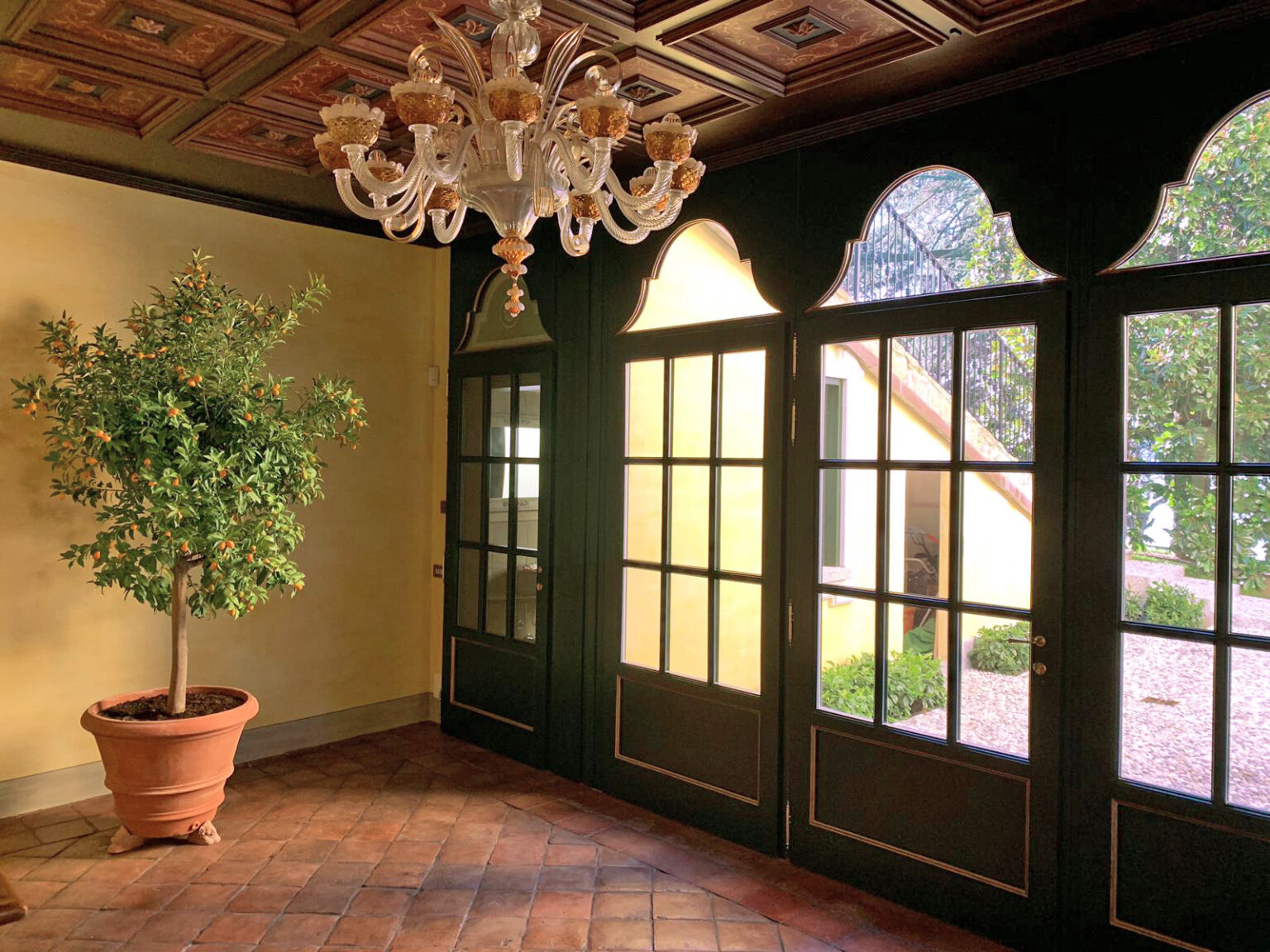 Interior view of a stylish room featuring a decorative chandelier, large glass doors, and a potted plant, with warm yellow walls and elegant architectural details. | Only on SopranoVillas
