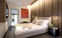 Modern bedroom featuring a minimalist design with a comfortable bed, wooden accent walls, and stylish decor. The room includes bedside tables with lamps and a vibrant piece of abstract art, creating a cozy and inviting atmosphere.