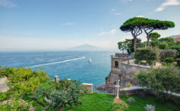 Scenic view of the coastline with lush greenery, overlooking the blue waters and a distant mountain, ideal for travel and nature enthusiasts.