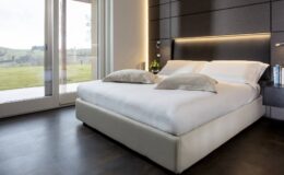 Modern bedroom interior featuring a stylish bed with white linens and decorative pillows, large windows allowing natural light, and a serene outdoor view. Ideal for showcasing contemporary home design and comfort.