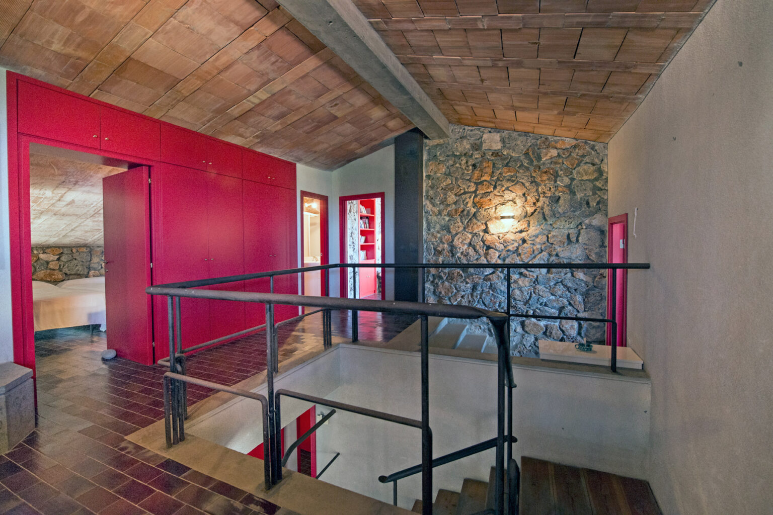 Interior view of a modern staircase with a metal railing, featuring stone and red accent walls in a well-lit space. The design showcases a blend of contemporary and rustic elements, highlighting the architectural details of the loft. | Only on SopranoVillas