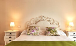 Elegant bedroom with a white ornate headboard, decorative floral pillows, a cozy green throw, and soft bedside lamps creating a warm ambiance.