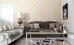 Modern living room with a patterned yellow and white accent wall, featuring a gray sofa, striped armchair, and a stylish coffee table with decorative items and magazines.
