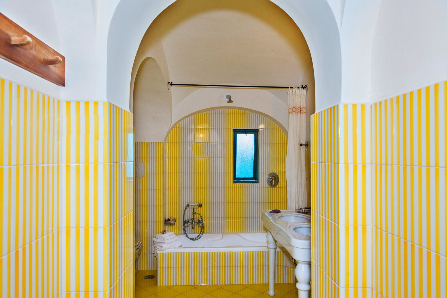 Brightly colored bathroom featuring yellow tiled walls, an arched entrance, a bathtub, and a small window for natural light. | Only on SopranoVillas