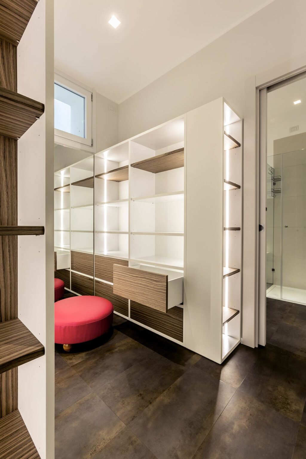Modern dressing area with sleek white shelving, wooden accents, and a vibrant red chair, featuring integrated lighting for enhanced visibility. | Only on SopranoVillas