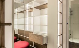 Modern dressing area with sleek white shelving, wooden accents, and a vibrant red chair, featuring integrated lighting for enhanced visibility.