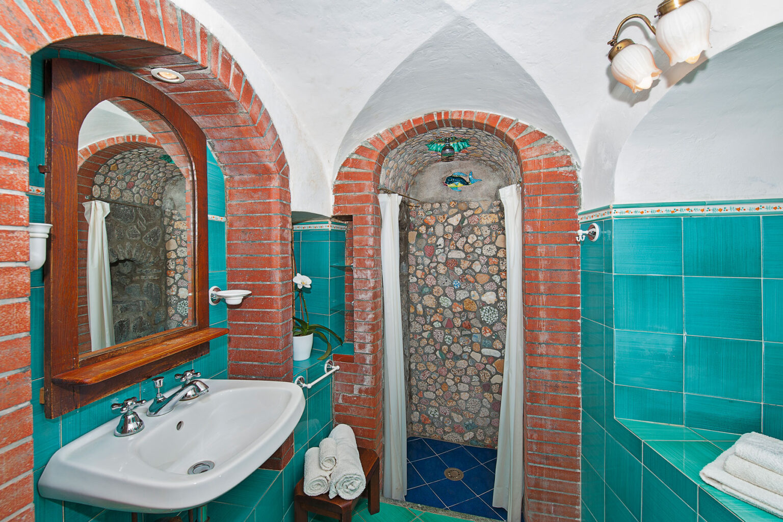 Elegant bathroom interior featuring turquoise tiles, a stone shower, and a wooden mirror. The design combines modern amenities with a rustic aesthetic, creating a serene atmosphere. | Only on SopranoVillas