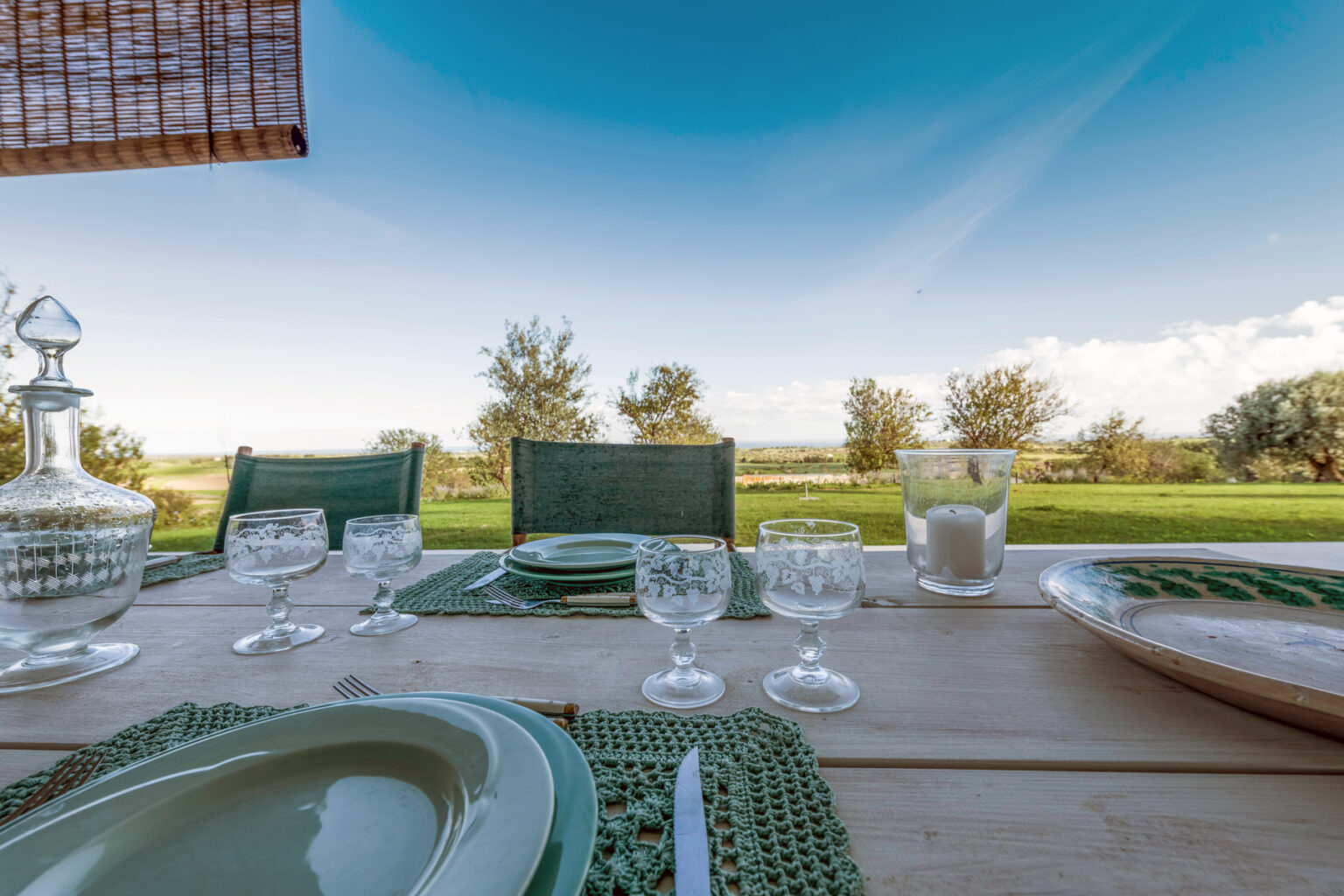 Outdoor dining setup with green plates and glasses on a wooden table, overlooking a scenic landscape with trees and a clear blue sky. Ideal for al fresco meals and gatherings. | Only on SopranoVillas