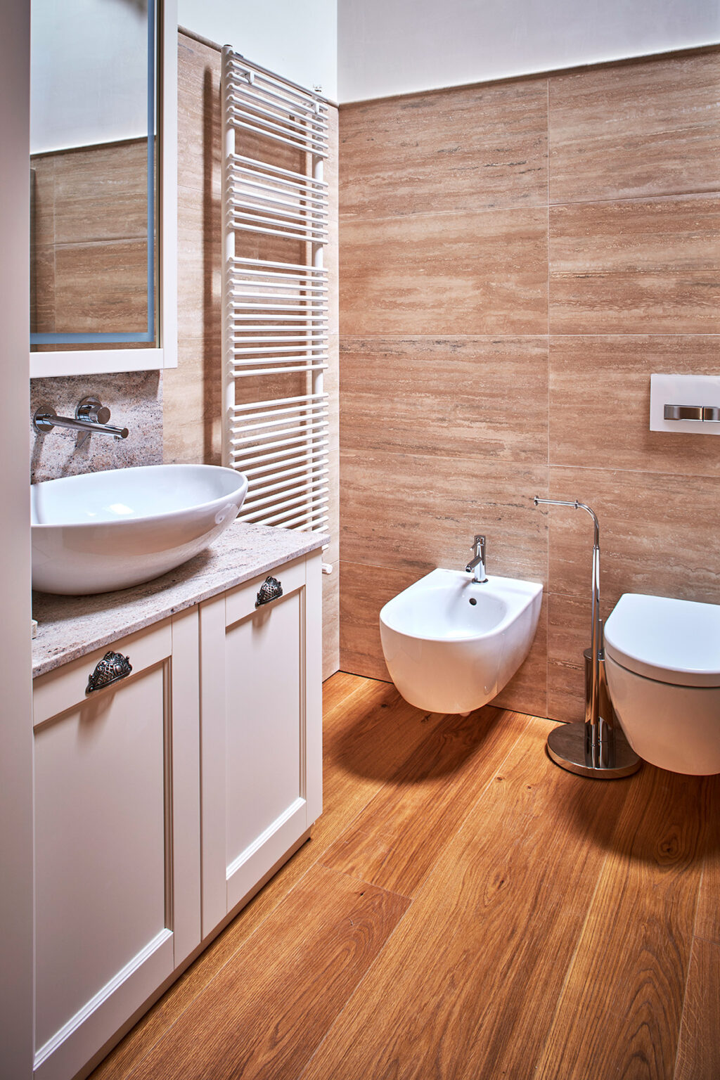 Modern bathroom interior featuring a stylish round sink, a wall-mounted bidet, and a sleek toilet. The warm wooden flooring complements the elegant beige wall tiles, creating a cozy yet sophisticated atmosphere. | Only on SopranoVillas