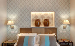 Elegant bedroom featuring a stylish headboard, decorative wall with a subtle pattern, two bedside lamps, and two decorative vases on a shelf, creating a cozy and inviting atmosphere.