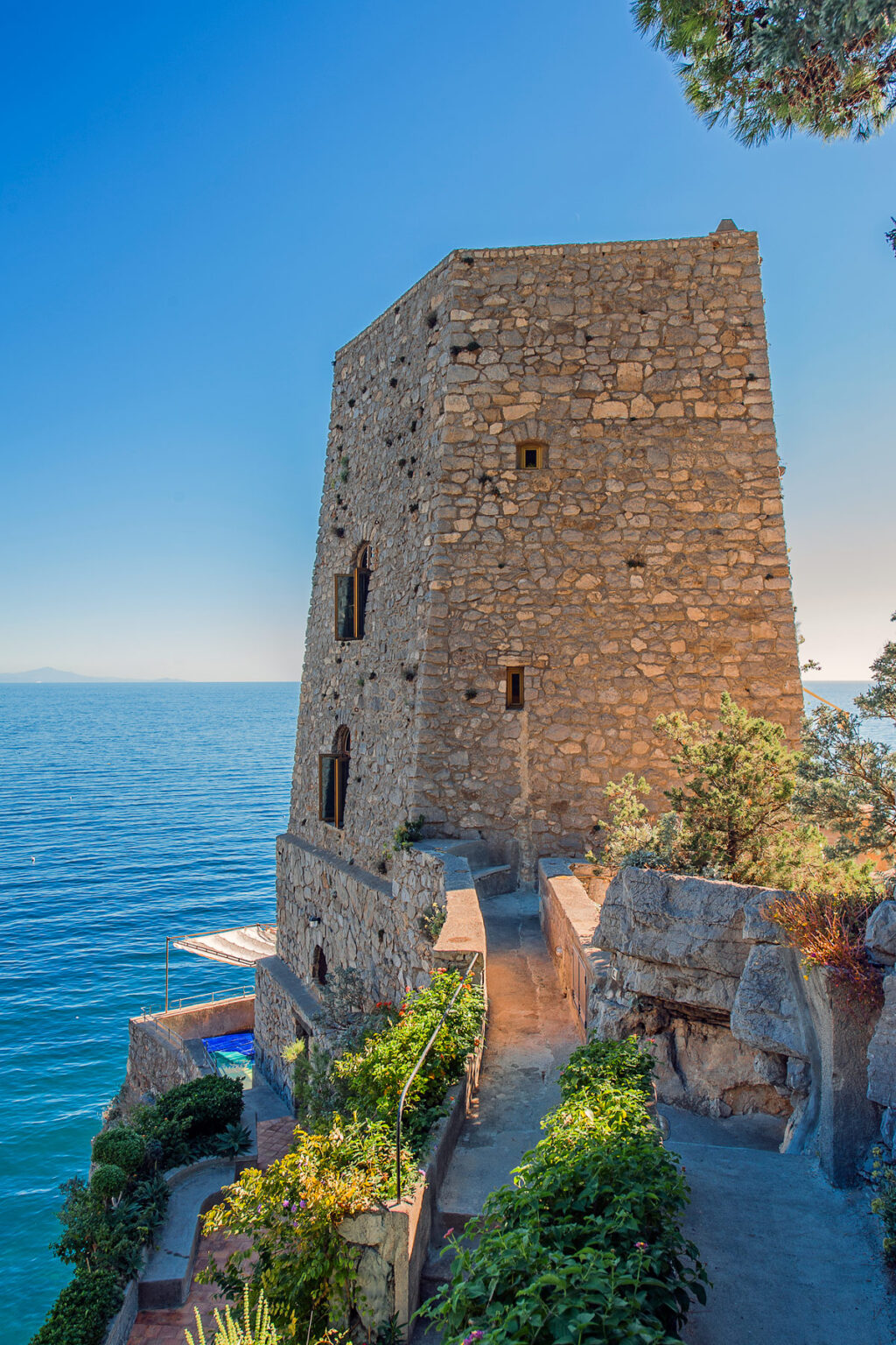 Stone tower overlooking the sea with clear blue waters and a bright sky, surrounded by greenery. Ideal for historical architecture enthusiasts and coastal scenery lovers. | Only on SopranoVillas