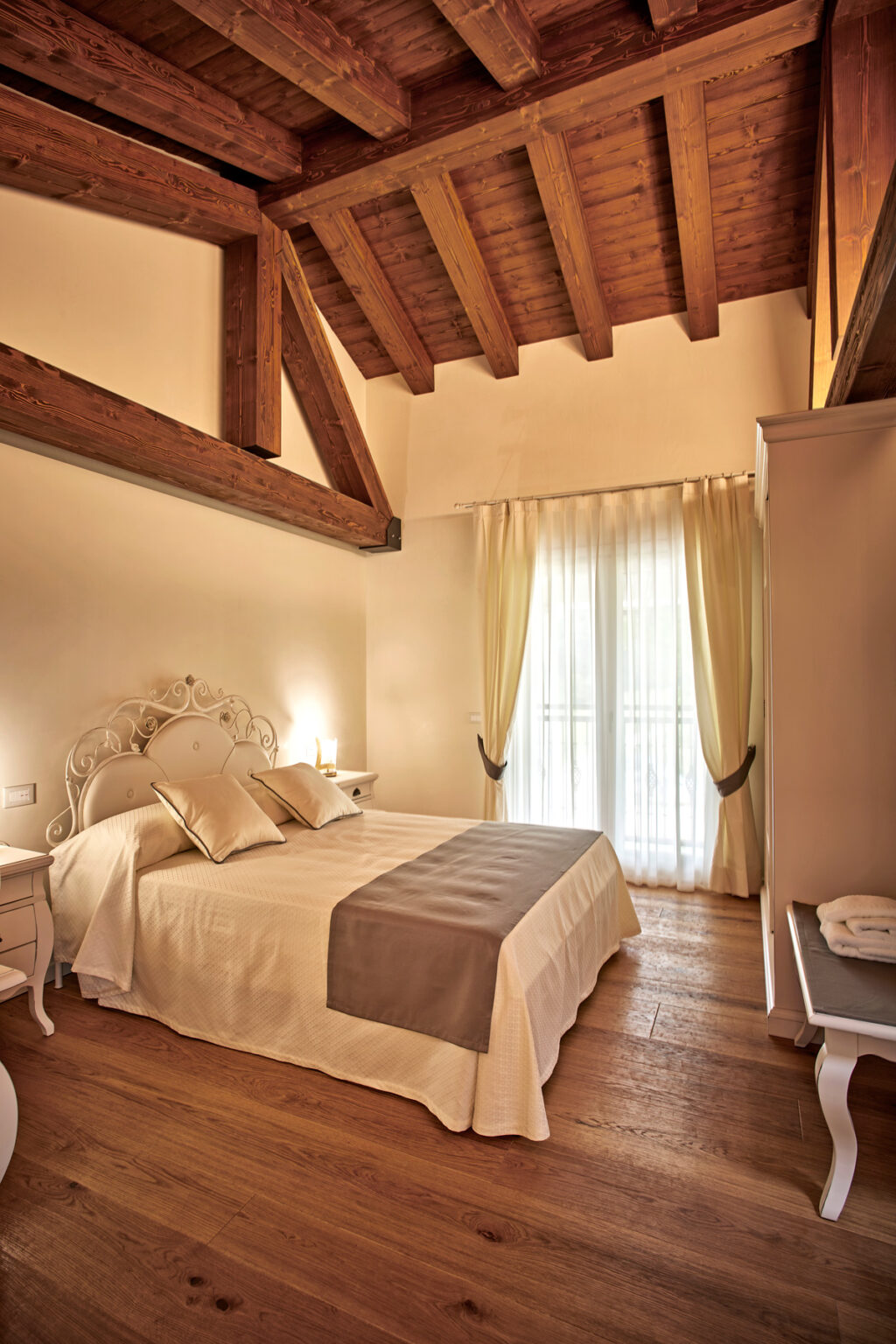 Cozy and elegantly decorated bedroom featuring a double bed with soft linens, wooden beams, and sheer curtains that allow natural light to fill the space. Perfect for a relaxing getaway. | Only on SopranoVillas